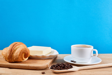 Coffee breakfast with croissant, butter and cup of black coffee on a oak wooden table.