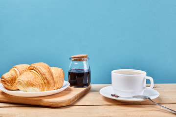breakfast with croissants.Fresh crispy croissants and coffee on a blue background and wooden table