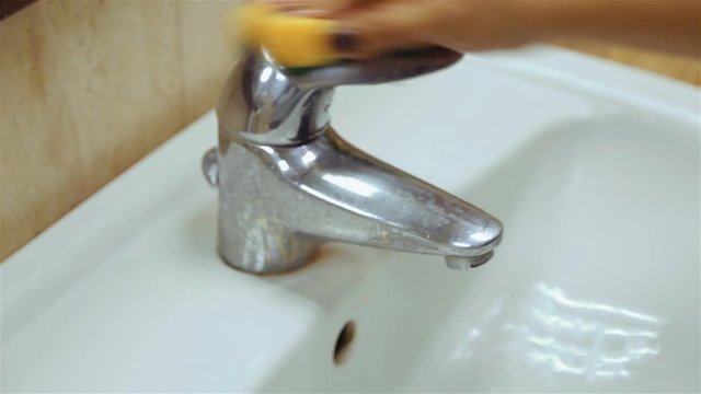 Woman cleaning water faucet with sponge. Handheld shot. Closeup.