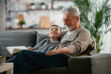 Grandfather and grandson reading a book. Grandpa and grandson  enjoying at home.