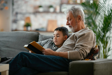 Grandfather and grandson reading a book. Grandpa and grandson  enjoying at home.