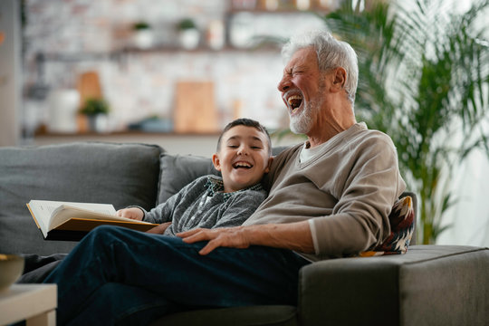 Grandfather and grandson reading a book. Grandpa and grandson enjoying at home.