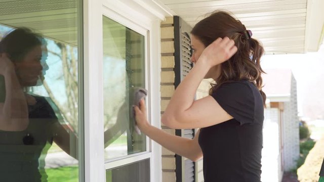 Attractive woman cleaning windows at her home outside during the day and doing some spring cleaning