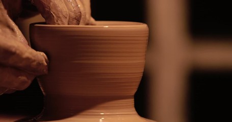 Young handsome sculptor shapes the clay product with pottery tools. Artisan potter prepares material for his pottery. Strong man hands working clay on potter's wheel. Work close-up.