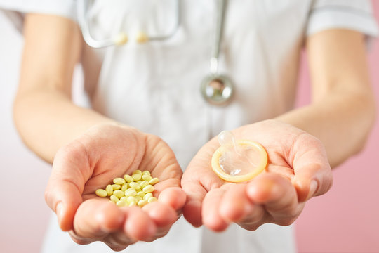 Female doctor holding condom for aids prevention and birth control pills. Contraceptives in hands for safe sex
