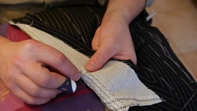 Tailor putting pad stitches in a suit's lapel run parallel to the lapel's roll line to accentuate its curvature