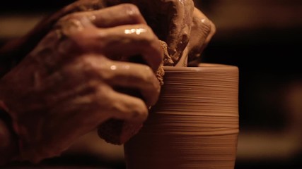 Young handsome sculptor shapes the clay product with pottery tools. Artisan potter prepares material for his pottery. Strong man hands working clay on potter's wheel. Work close-up.