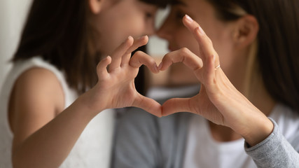 Close up of young mother and cute little daughter make heart sign with hands enjoy close tender...