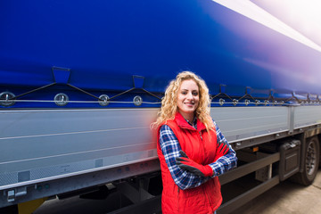 Portrait of female trucker with crossed arm proudly standing by her truck vehicle ready for...