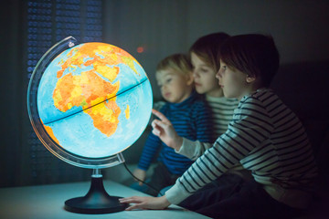 Little children, brothers, looking at illuminated globe, exploring