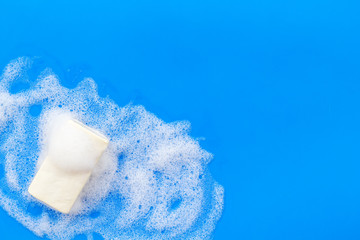 Soap bar with foam on blue background top-down copy space