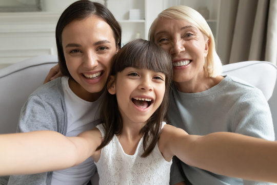 Close up portrait of overjoyed three generations of women have fun at home make selfie together, smiling little girl with young mom and senior grandmother take self-portrait picture on camera