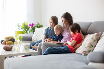 Young woman, mother with three kids, reading a book at home, hugging and laughing