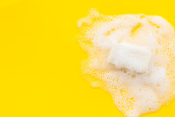 Soap bar with foam on yellow background top-down copy space