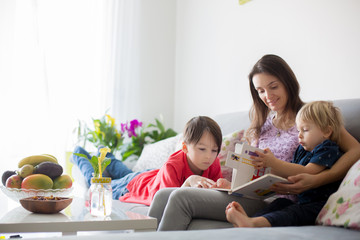 Young woman, mother with three kids, reading a book at home, hugging and laughing