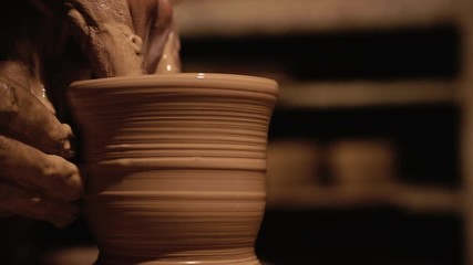 Young handsome sculptor shapes the clay product with pottery tools. Artisan potter prepares material for his pottery. Strong man hands working clay on potter's wheel. Work close-up.