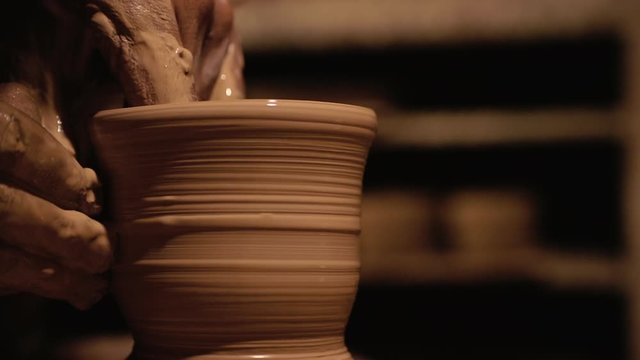 Young handsome sculptor shapes the clay product with pottery tools. Artisan potter prepares material for his pottery. Strong man hands working clay on potter's wheel. Work close-up.