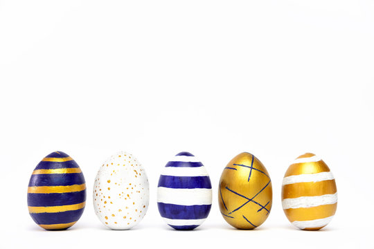 Five easter eggs trendy colored classic blue, white and golden decorated on white table. Happy Easter card with copy space for text. Minimal style.