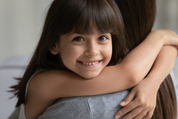 Portrait of cute smiling little girl hug make peace reconcile with young mother at home, small...