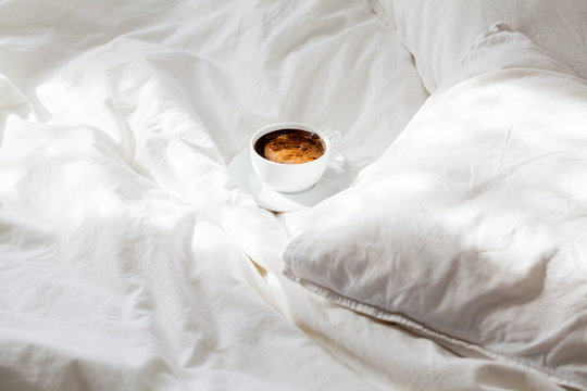 White cup of coffee in white bed. Work from home concept.
