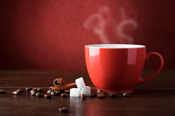 A red cup of coffee on wooden desk with coffee bean and sugar