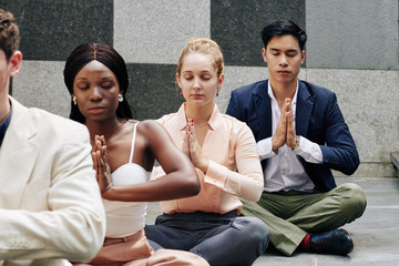 Calm young multi-ethnic business people holding hands in namaste mudra after meditation practice