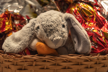 Obraz premium Plush rabbit in wicker basket with chocolate eggs for Easter party