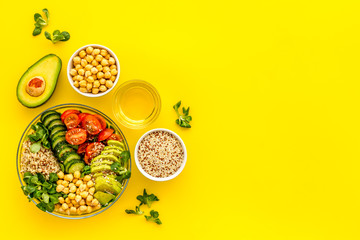 Vegan bowl. Avocado, quinoa, tomato, spinach and chickpeas vegetables salad on yellow table top-down copy space