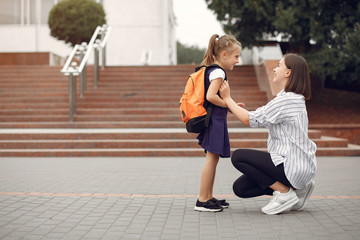 Mother and daughter. Family standing near school. Mom accompanies her child to school