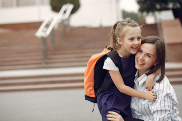 Mother and daughter. Family standing near school. Mom accompanies her child to school