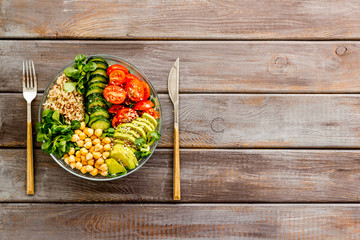 Veggie bowl. Vegetable salad with quinoa, avocado, tomato, spinach and chickpeas - on wooden table. Top view copy space