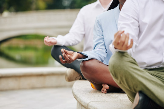 Cropped image of young business people sitting in lotus position keeping hands in shuni mudra