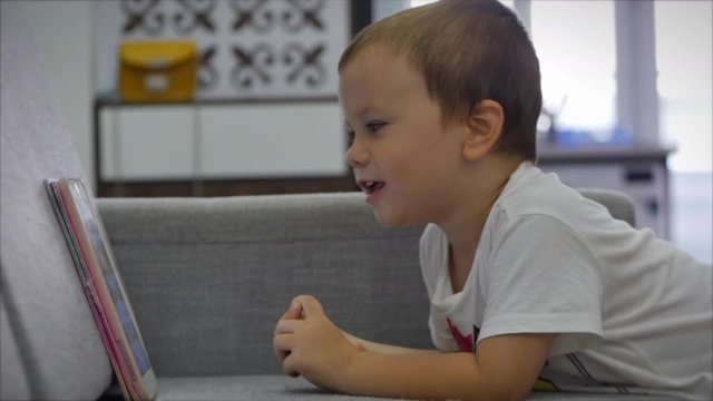 Curious cute preschool kid girl using digital tablet technology device lying on carpet floor alone. Small child hold pad computer surfing internet play game at home. Children tech addiction concept