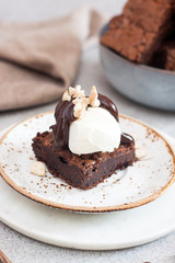 Homemade brownie with scoop of vanilla ice cream, chocolate sauce and nuts. Gray background