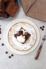 Homemade brownie with scoop of vanilla ice cream, chocolate sauce and nuts. Gray background