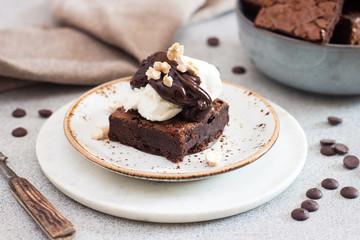 Homemade brownie with scoop of vanilla ice cream, chocolate sauce and nuts. Gray background