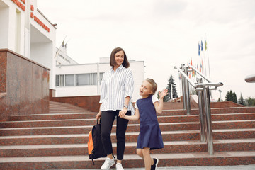 Mother and daughter. Family standing near school. Mom accompanies her child to school