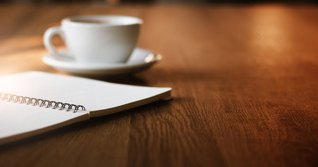 Close up of blank notebook with white cup of coffee on wooden table