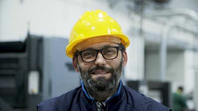 Closeup view of smiling professional engineer looking at camera. Cheerful mature engineer posing at factory. Manufacturing employee concept