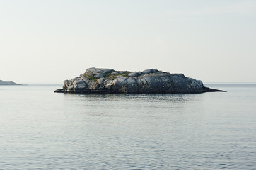 Uninhabited small isle with smooth granite rocks and green moss, lichen in blue Arctic Ocean in...