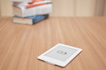 e-reader, kindle, with low battery symbol, in the background a stack of unfocused books