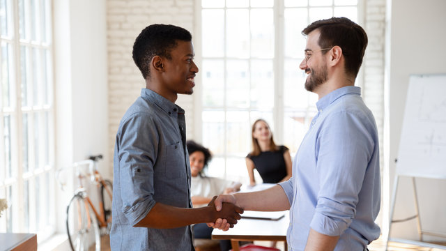 Diverse businesspeople gather in boardroom company boss handshake subordinate african staff member praising best employee of month, express gratitude for outstanding work, promotion and reward concept