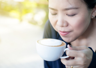 Asian girl smelling and enjoying cup of hot coffee at the outside of cafe. with sunlight effect.