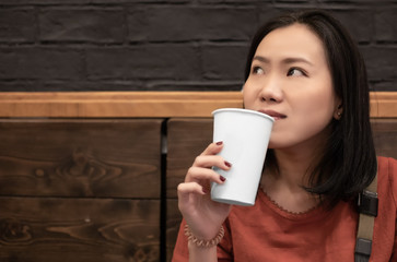 Asian young woman drinking a fresh white paper cup of water or other beverage.