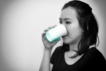 Asian young woman drinking a fresh white paper cup of water or other beverage.bllack and white tone