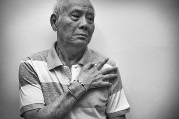 Elderly Asian man put his hand on his shoulder because of shoulder pain or muscle pain. Black and...