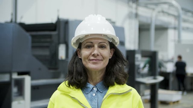 Front view of smiling female technician looking at camera. Cheerful mature engineer posing at factory. Manufacturing employee concept