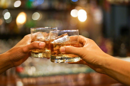 Two men clinking glasses of whiskey drink alcohol beverage together at counter in the pub                    