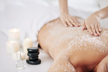 Beautician exfoliating back of client with sea salt and massage oil