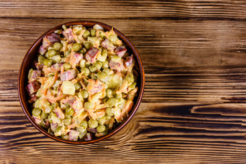 Salad with sausage, green pea, onion and carrot in glass bowl on wooden table. Top view